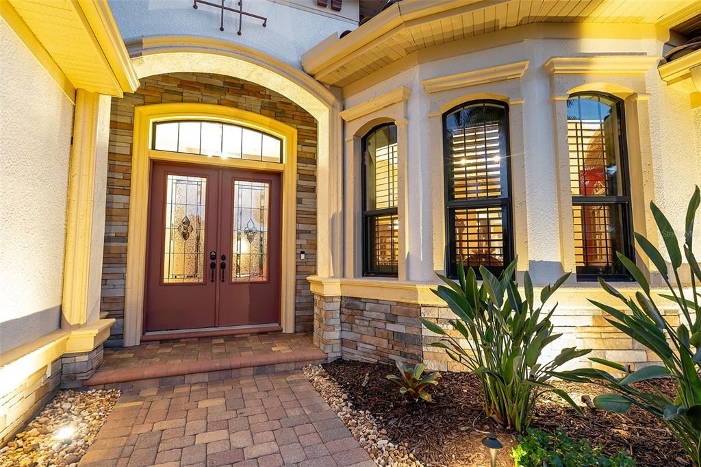 A stone-accented entryway features a double front door with glass panels and arched windows — 15114 LINN PARK TERRACE, LAKEWOOD RANCH, FL