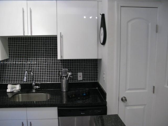 A kitchen features white cabinets, a black tiled backsplash, a stainless steel sink, and dark countertops — 1525 Meridian Ave # 207, Miami Beach FL 33139, MIAMI BEACH, FL