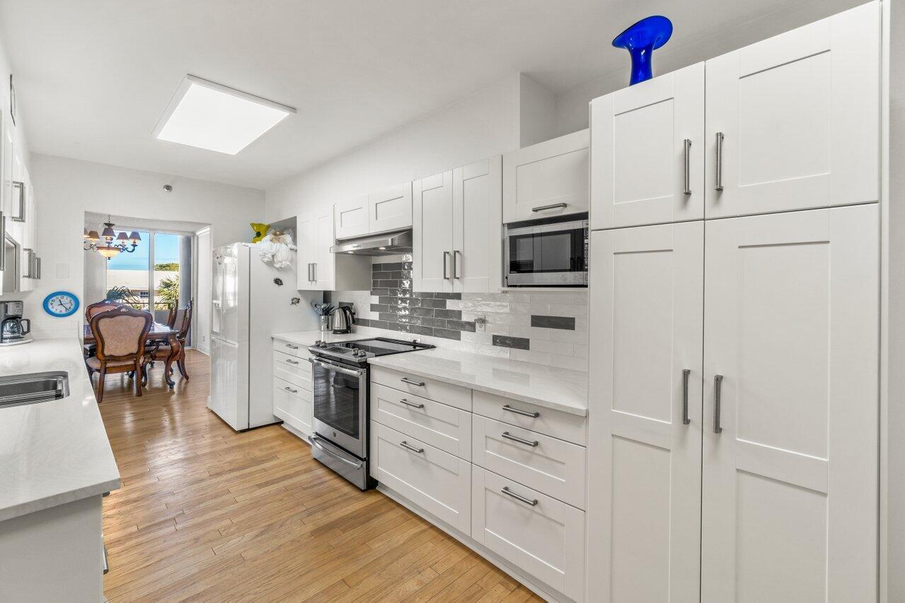 A modern kitchen features white cabinetry, stainless steel appliances, gray subway tile backsplash, and wood flooring — 1401 S Ocean Boulevard # 3090, Boca Raton FL 33432, BOCA RATON, FL