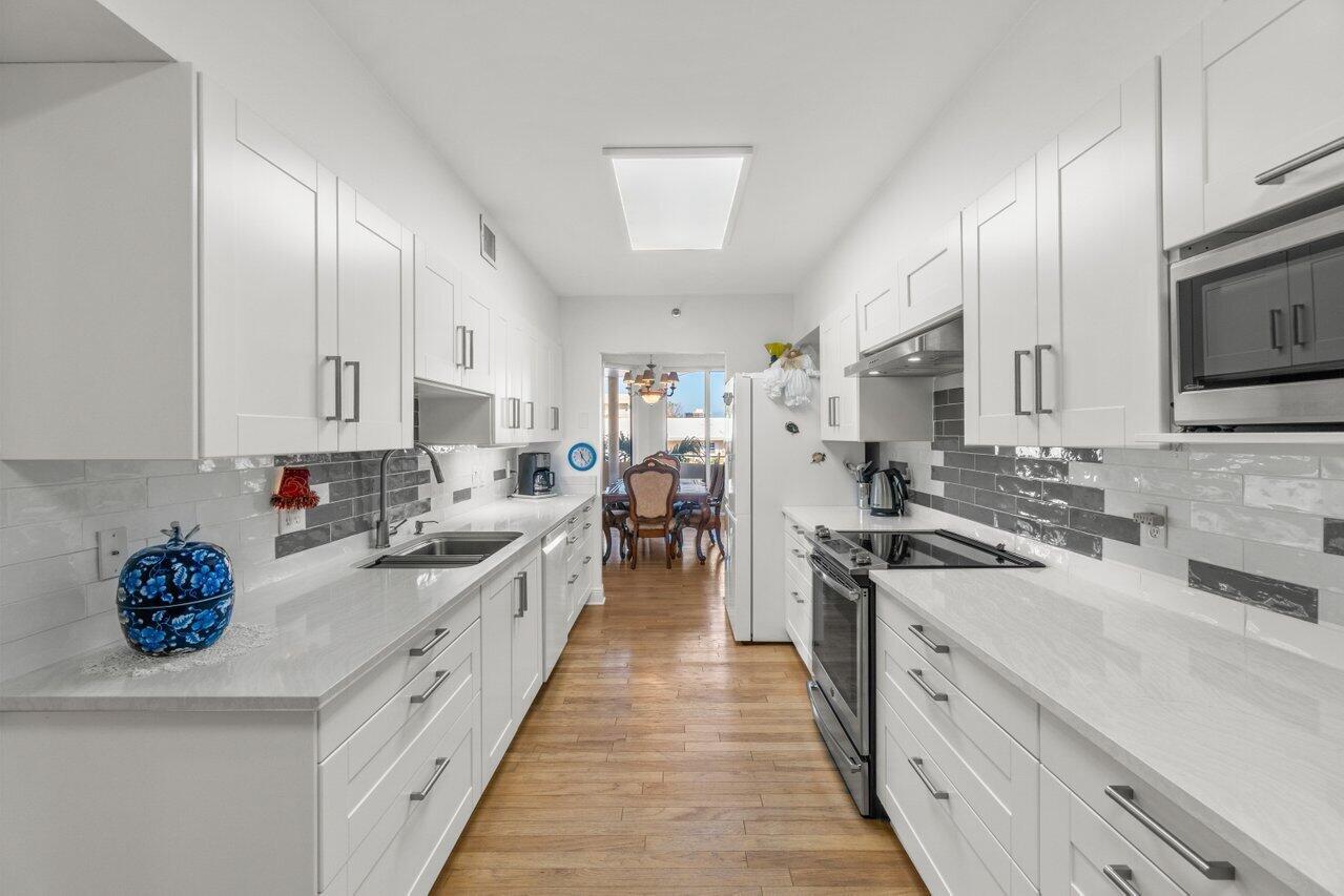 A galley kitchen features white cabinets, quartz countertops, gray subway tile backsplash, and wood flooring — 1401 S Ocean Boulevard # 3090, Boca Raton FL 33432, BOCA RATON, FL