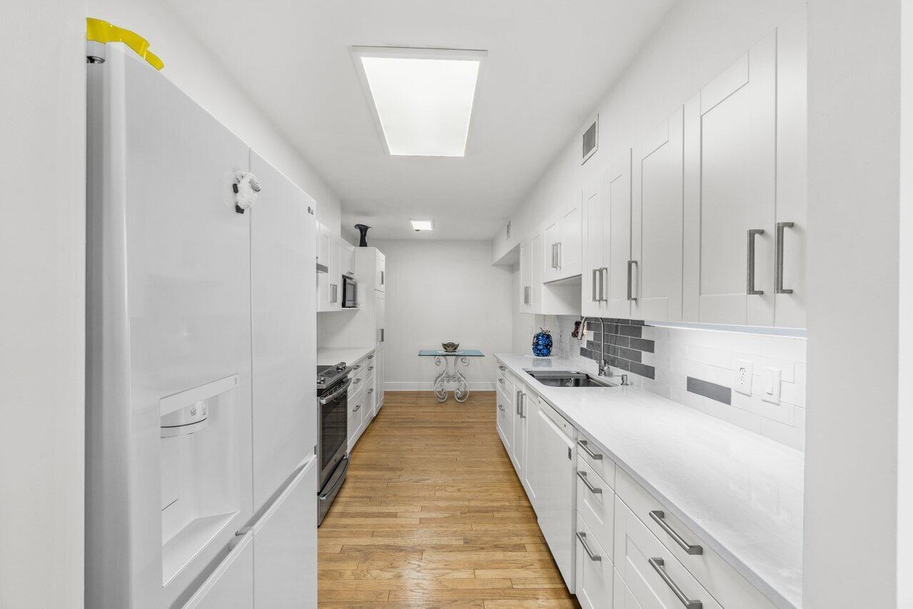 A narrow galley kitchen features white cabinetry, stainless steel appliances, and light wood flooring — 1401 S Ocean Boulevard # 3090, Boca Raton FL 33432, BOCA RATON, FL