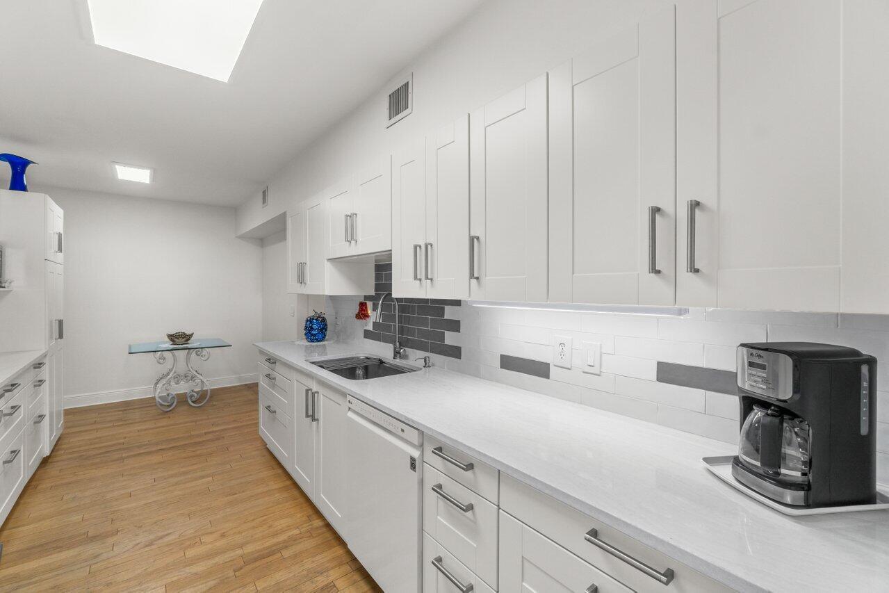 A modern kitchen features white cabinets, light countertops, a gray tile backsplash, and wood flooring — 1401 S Ocean Boulevard # 3090, Boca Raton FL 33432, BOCA RATON, FL