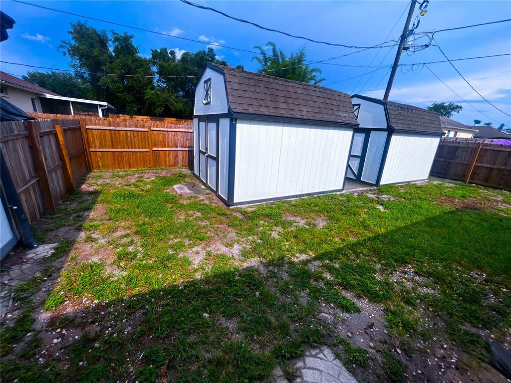 A backyard features two white storage sheds with dark trim sitting on patchy grass — 3055 KIRKLAND STREET, DELTONA, FL