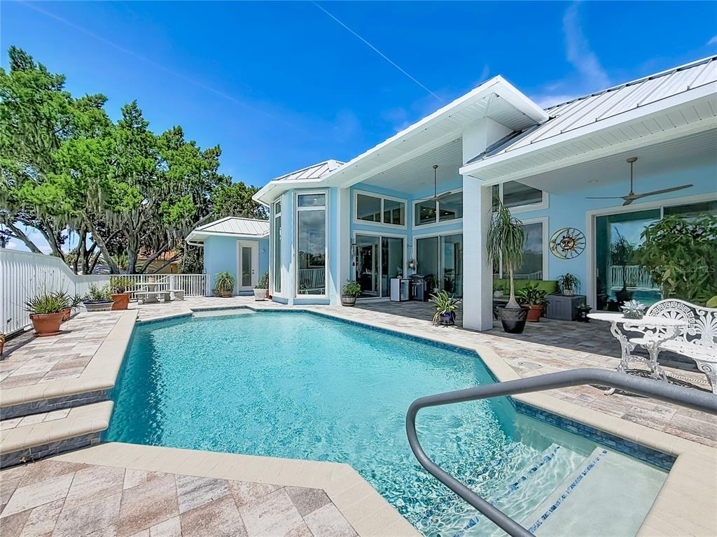 A swimming pool sits on a stone patio outside a light blue house with white trim — 838 SW KINGS BAY DRIVE, CRYSTAL RIVER, FL