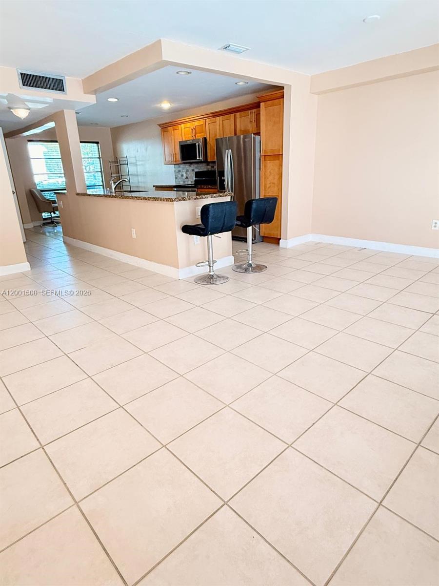 An open-concept kitchen features wooden cabinets, stainless steel appliances, and a breakfast bar with stools — 2750 N 34th Ave # 9D, Hollywood FL 33021, HOLLYWOOD, FL