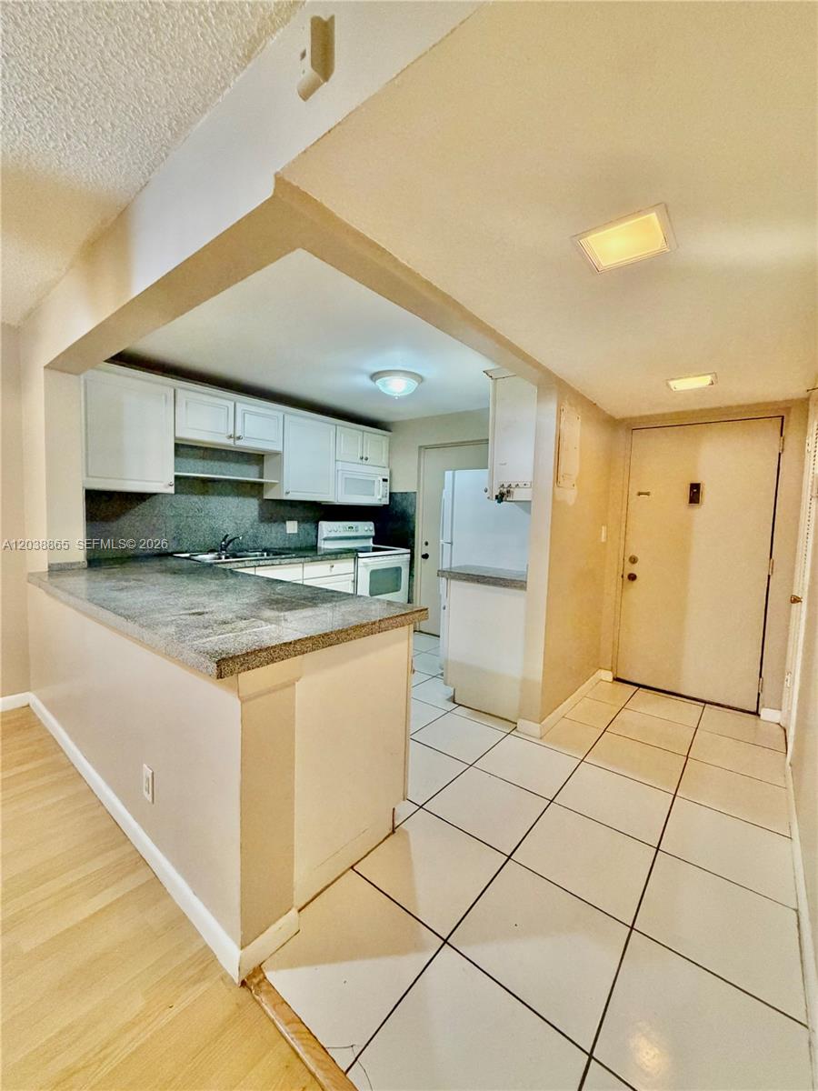 A kitchen with white cabinets, granite countertops, and tile flooring opens to an entryway — 2320 S Cypress Bend Dr # 206, Pompano Beach FL 33069, POMPANO BEACH, FL