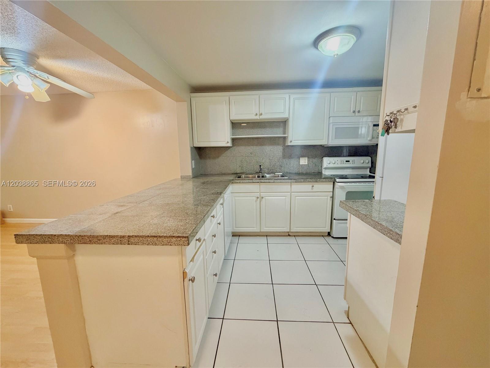 A kitchen features white cabinets, granite countertops, and white tile flooring — 2320 S Cypress Bend Dr # 206, Pompano Beach FL 33069, POMPANO BEACH, FL