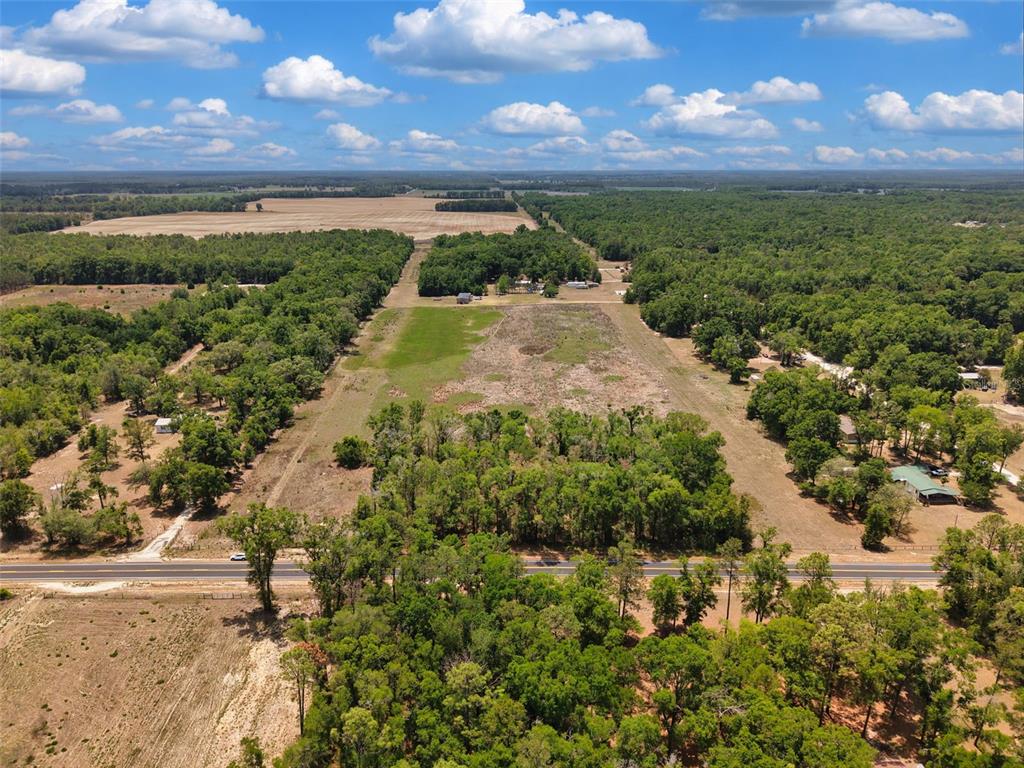 An aerial view shows a large, partially cleared grassy lot bordered by trees and a road — 18 AC NW CR 138, BRANFORD, FL