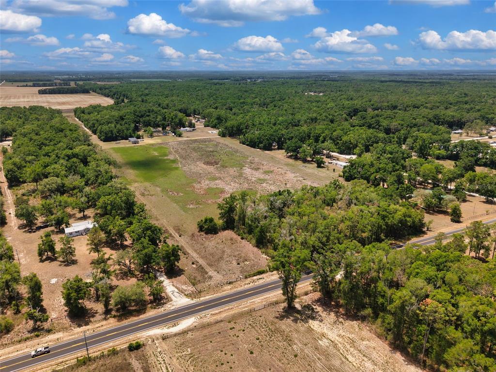 An aerial view shows a large, grassy lot bordered by trees and a paved road — 18 AC NW CR 138, BRANFORD, FL