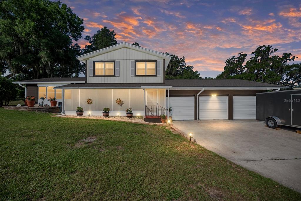 A two-story house with a screened-in porch, three-car garage, and a concrete driveway at dusk — 30 EMERALD RUN, OCALA, FL