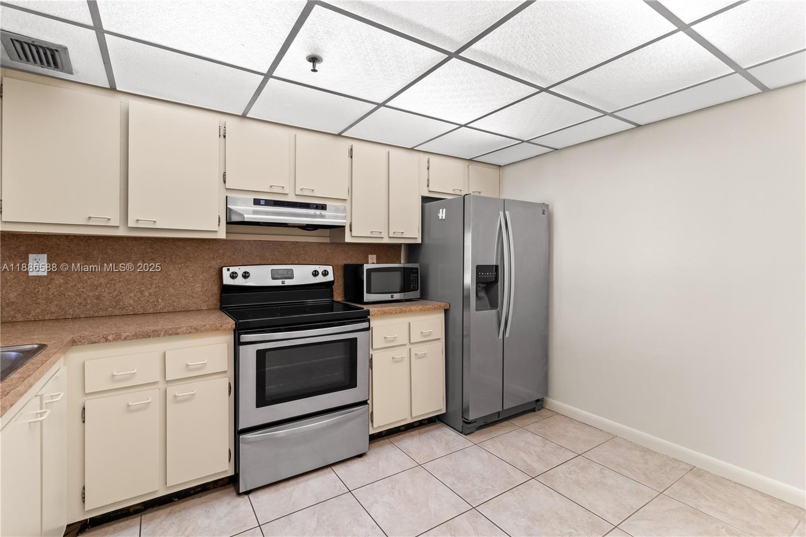 A kitchen features beige cabinets, laminate countertops, stainless steel appliances, and a drop ceiling — 2625 Collins Ave # 608, Miami Beach FL 33140, MIAMI BEACH, FL