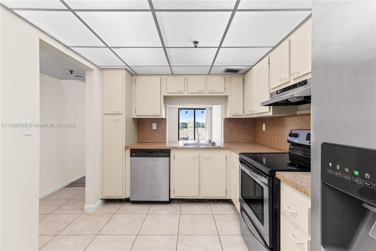 A kitchen features beige cabinets, stainless steel appliances, a drop ceiling, and tiled flooring — 2625 Collins Ave # 608, Miami Beach FL 33140, MIAMI BEACH, FL
