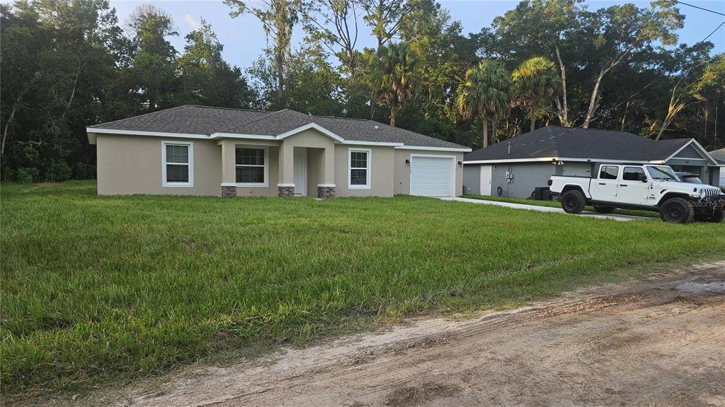 A single-story tan house with a white garage and a large grassy front yard — 3745 SE 133RD PLACE, BELLEVIEW, FL