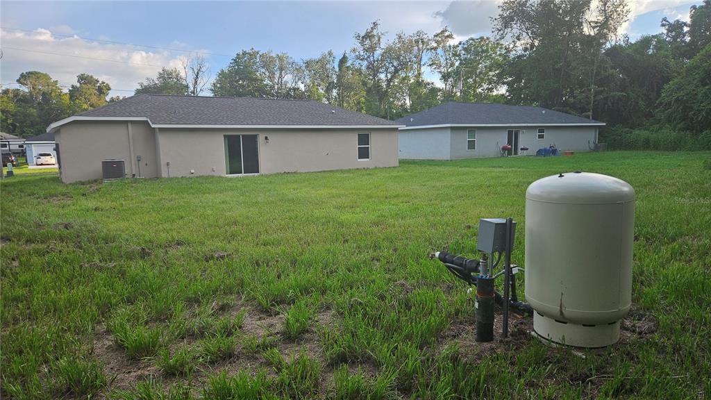 A backyard view showing two houses and a well water pressure tank in the foreground — 3745 SE 133RD PLACE, BELLEVIEW, FL
