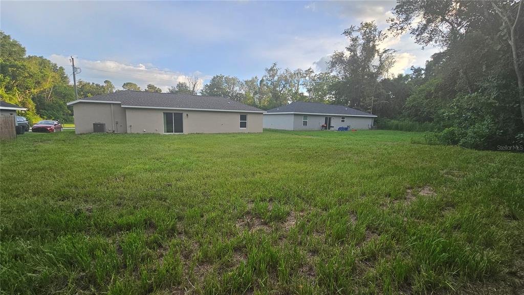A grassy backyard view of the rear exteriors of two single-story suburban houses — 3745 SE 133RD PLACE, BELLEVIEW, FL