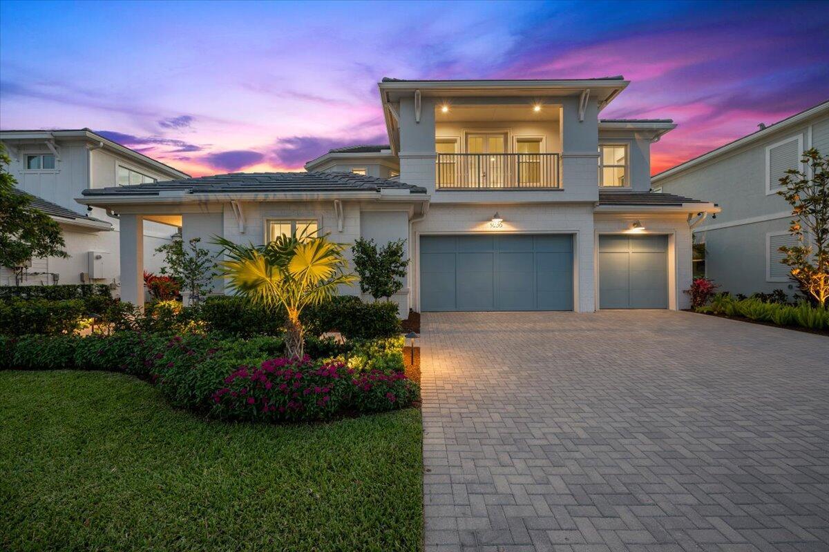 A two-story house with a blue garage, a balcony, and a paved driveway at dusk — 9236 Crestview Circle, Palm Beach Gardens FL 33412, PALM BEACH GARDENS, FL