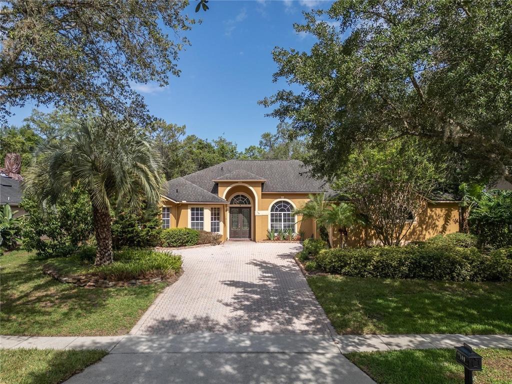 A single-story house with a paved driveway, arched entryway, and mature trees in the yard — 140 SEVILLE CHASE DRIVE, WINTER SPRINGS, FL