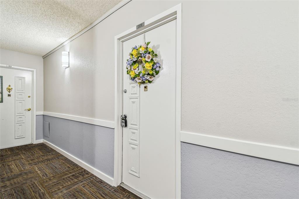 A hallway features two white apartment doors with wreaths and gray wainscoting — 17920 GULF BOULEVARD UNIT 208, REDINGTON SHORES, FL