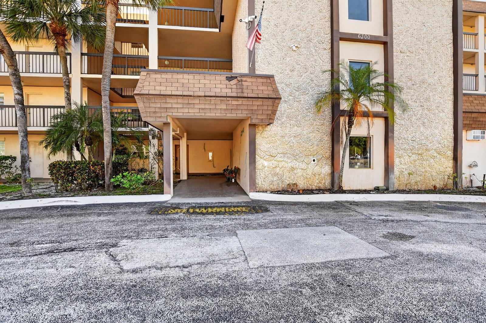 The exterior of a multi-story apartment building features a covered entrance and palm trees — 6300 NW 2nd Avenue # 306, Boca Raton FL 33487, BOCA RATON, FL