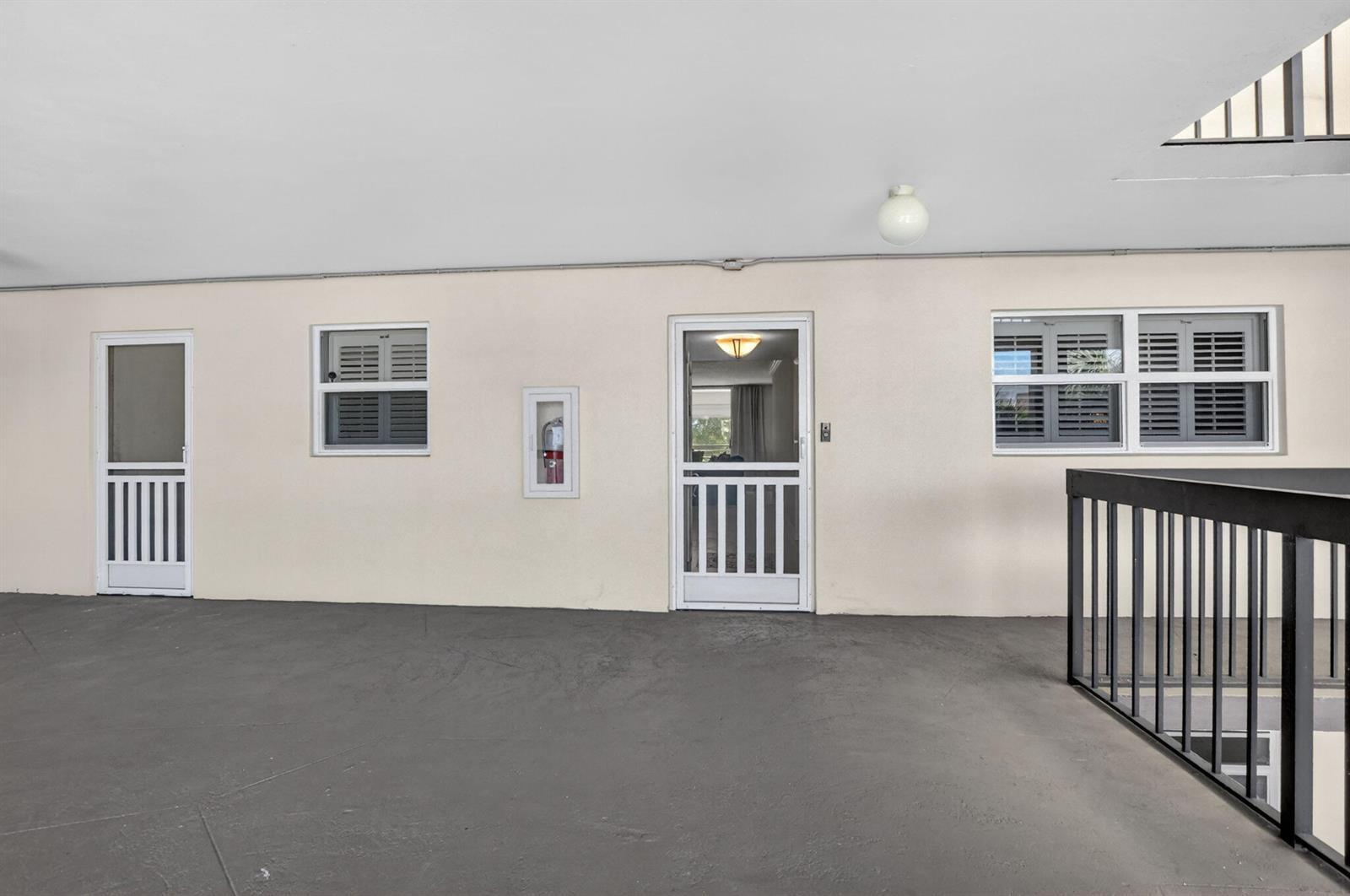 An exterior walkway with a grey floor, two screen doors, windows, and a fire extinguisher — 6300 NW 2nd Avenue # 306, Boca Raton FL 33487, BOCA RATON, FL
