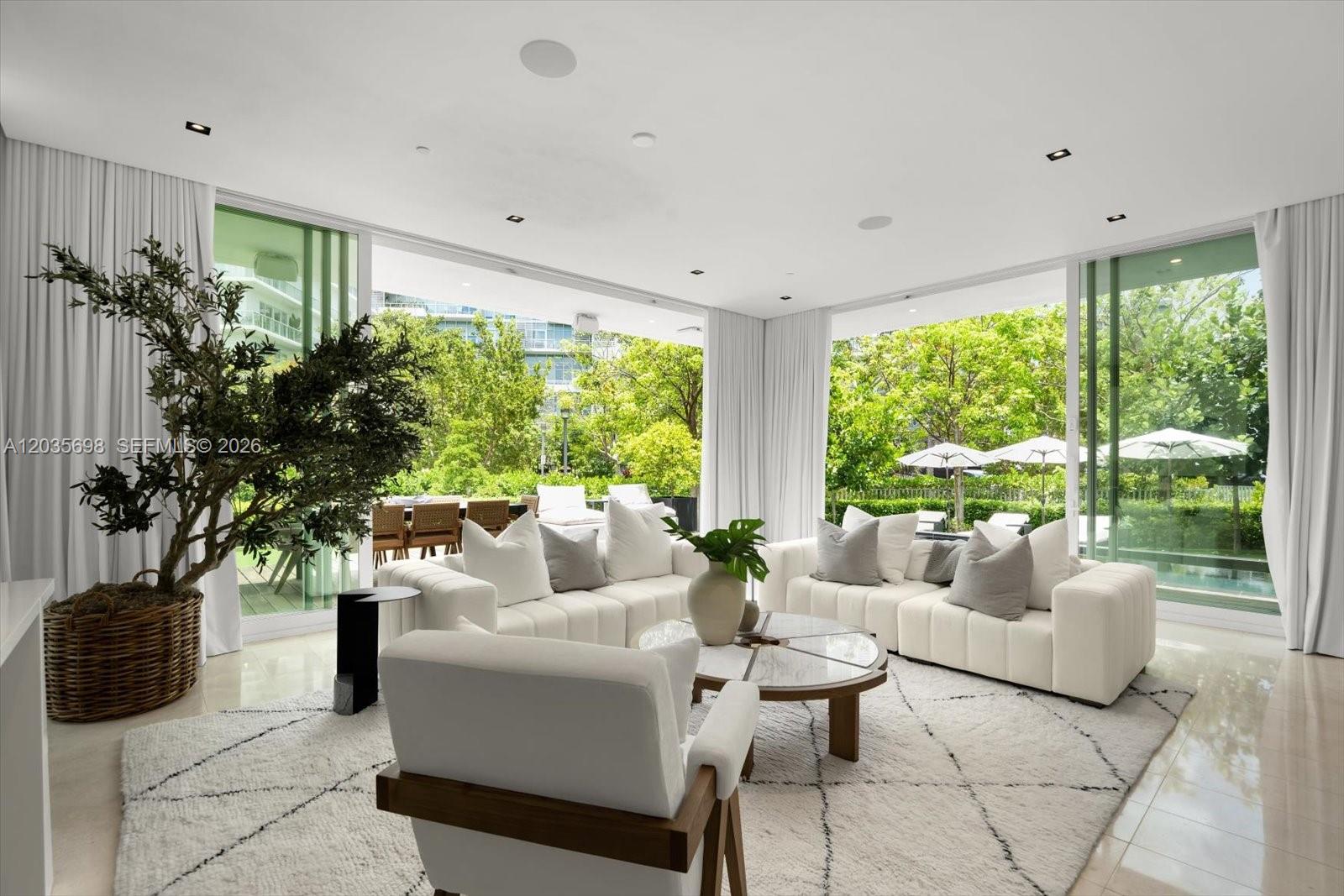 A bright living room features white sofas, a patterned rug, and floor-to-ceiling glass doors — 810 W 47 CT, Miami Beach FL 33140, MIAMI BEACH, FL