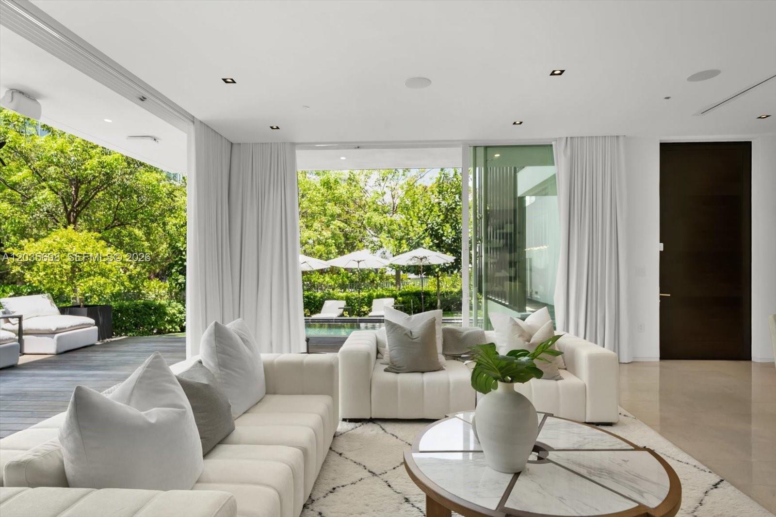 A modern living room features white sofas, a marble coffee table, and floor-to-ceiling glass doors — 810 W 47 CT, Miami Beach FL 33140, MIAMI BEACH, FL