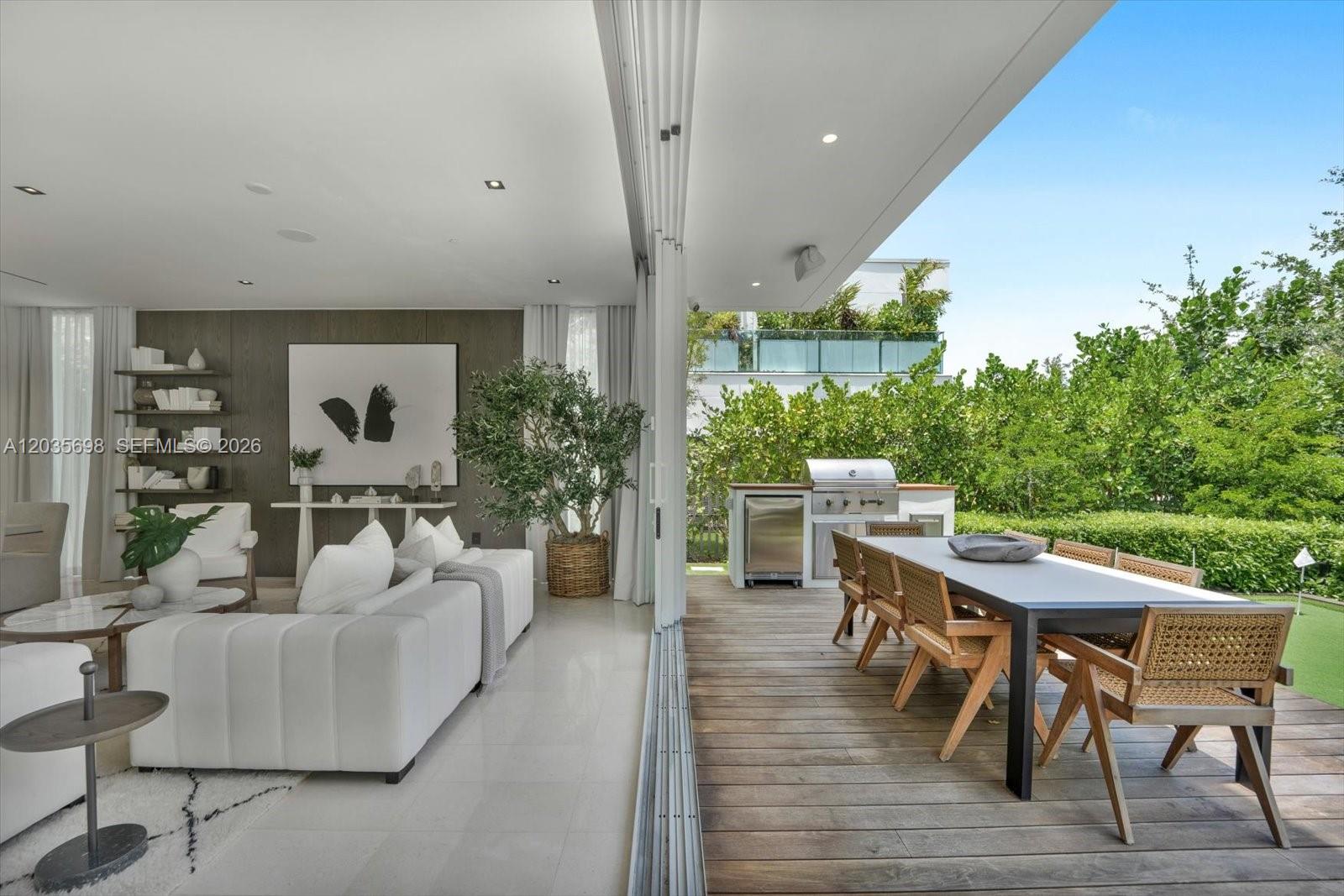 An indoor living area opens to a wooden deck with an outdoor kitchen and dining table — 810 W 47 CT, Miami Beach FL 33140, MIAMI BEACH, FL