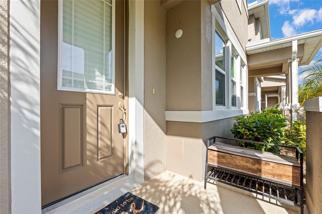A brown front door with a lockbox sits beside a small wooden bench and bushes — 13366 ABUELA ALLEY, WINDERMERE, FL