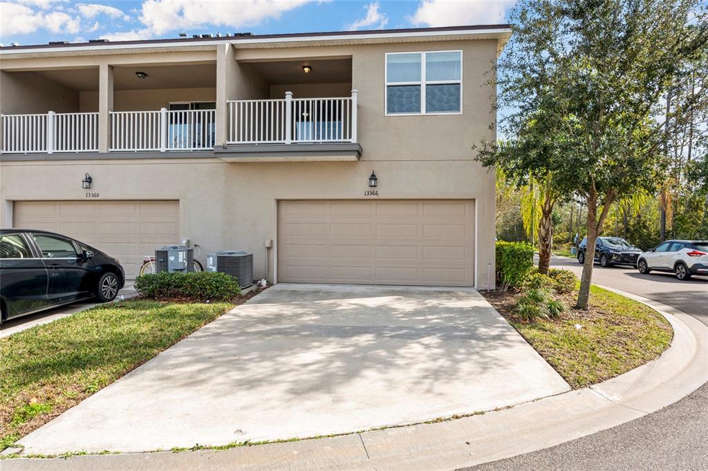 A two-story townhouse exterior features a beige garage, a concrete driveway, and a second-floor balcony — 13366 ABUELA ALLEY, WINDERMERE, FL