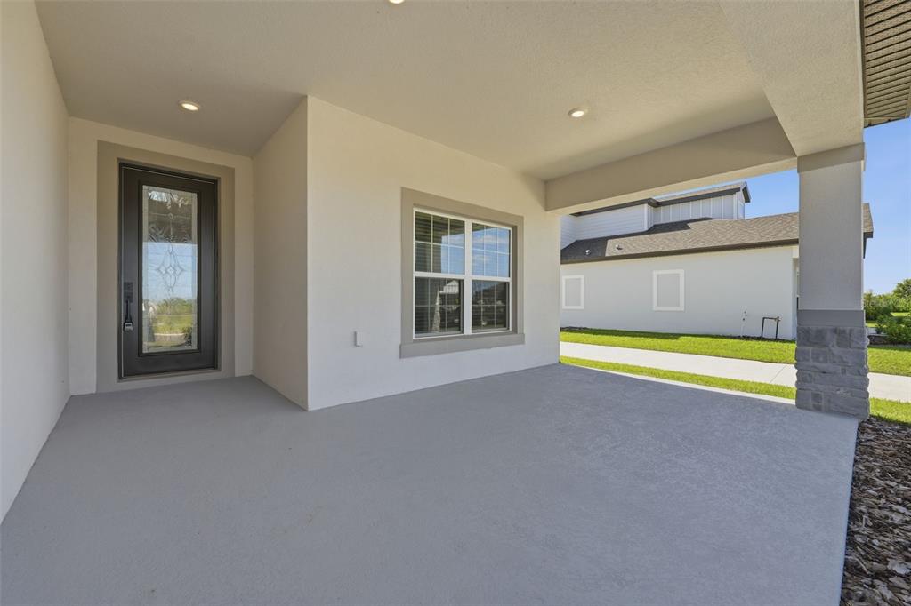 A covered concrete patio features a dark glass-paneled door, a window, and a stone pillar — 3339 CHINOTTO DRIVE, LAKE ALFRED, FL