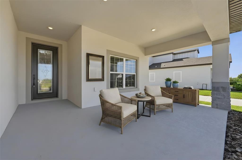 A covered concrete patio features two wicker chairs, a small table, and a wooden console — 3339 CHINOTTO DRIVE, LAKE ALFRED, FL