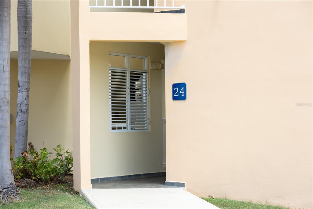 An exterior view of a building entrance with a blue number 24 sign — PR-713 KM 2.5 COND. EL LEGADO GOLF RESORT UNIT 2412, GUAYAMA, PR