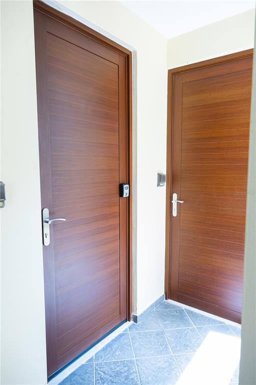 Two wooden doors with horizontal grain and silver handles are set in a tiled entryway — PR-713 KM 2.5 COND. EL LEGADO GOLF RESORT UNIT 2412, GUAYAMA, PR