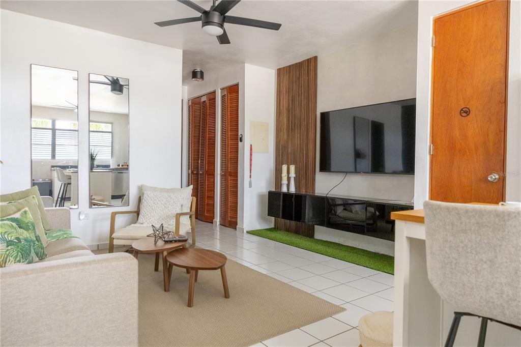 A living room features a wall-mounted television, wood-slat accent wall, and a beige area rug — PR-713 KM 2.5 COND. EL LEGADO GOLF RESORT UNIT 2412, GUAYAMA, PR