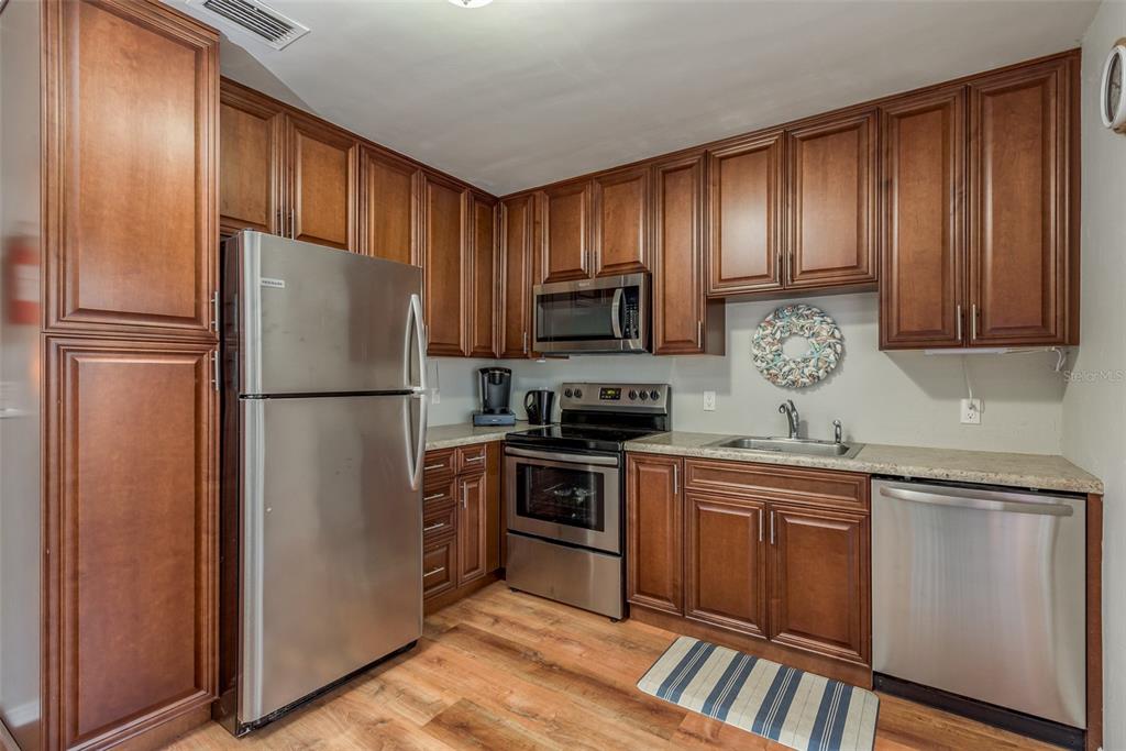 A kitchen features wood cabinets, stainless steel appliances, and light-colored countertops over wood-look flooring — 1253 UNION STREET, CLEARWATER, FL