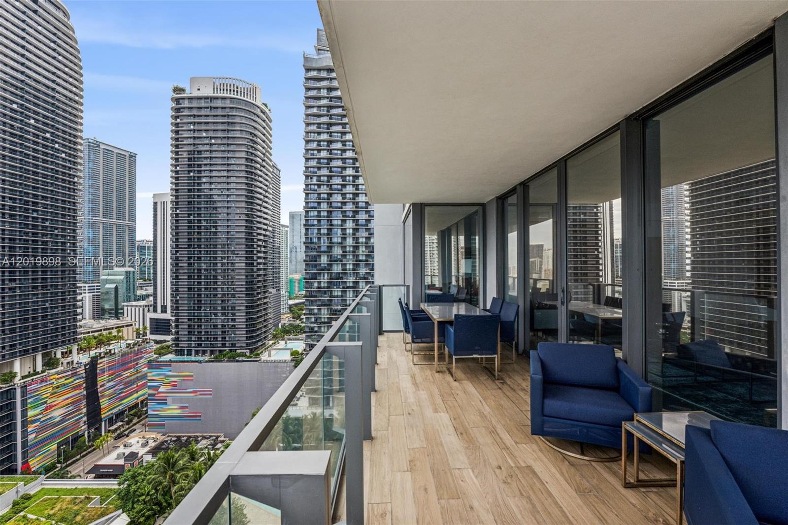 A high-rise balcony features wood-look tile flooring, blue outdoor furniture, and views of city skyscrapers — 88 SW 7th St # 2111, Miami FL 33130, MIAMI, FL