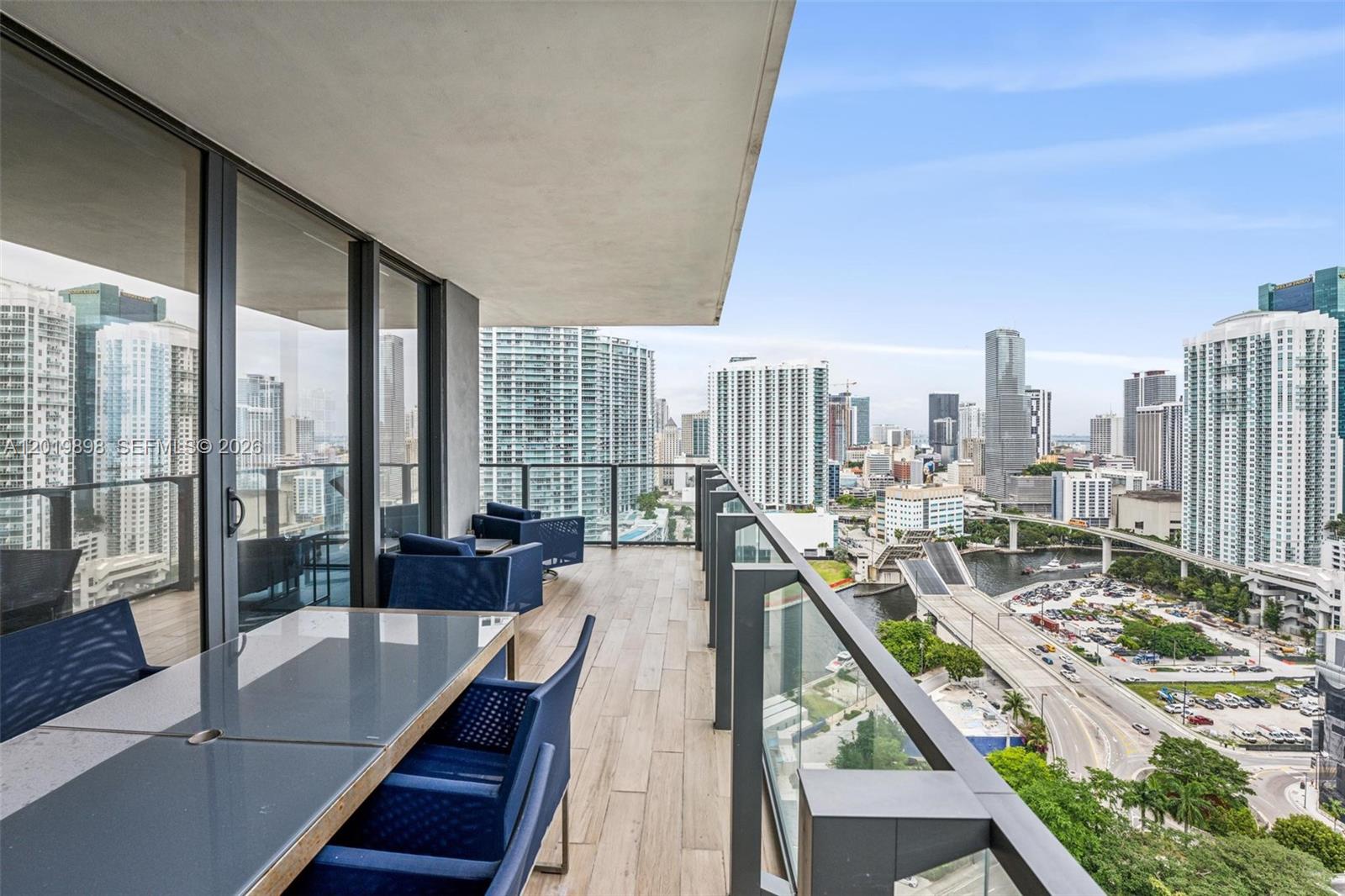 A high-rise balcony features outdoor furniture, wood-look tile flooring, and a panoramic city view — 88 SW 7th St # 2111, Miami FL 33130, MIAMI, FL