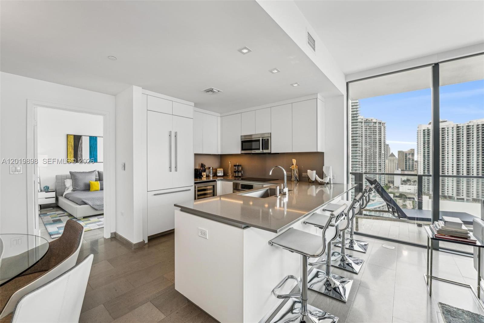 A modern kitchen features white cabinetry, gray countertops, and a breakfast bar with metal stools — 88 SW 7th St # 2111, Miami FL 33130, MIAMI, FL