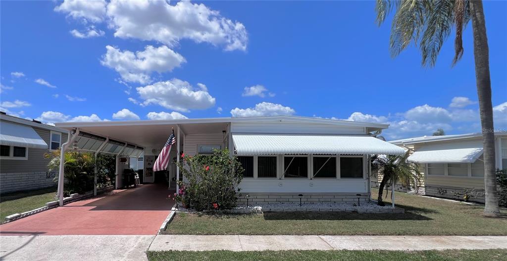 A single-story manufactured home with a carport, an American flag, and a white awning — 1100 BELCHER ROAD S UNIT 260, LARGO, FL