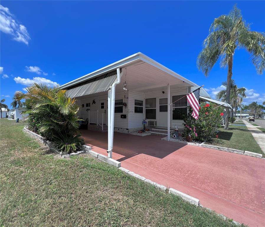 A white mobile home features a covered carport, a front porch, and a palm tree — 1100 BELCHER ROAD S UNIT 260, LARGO, FL
