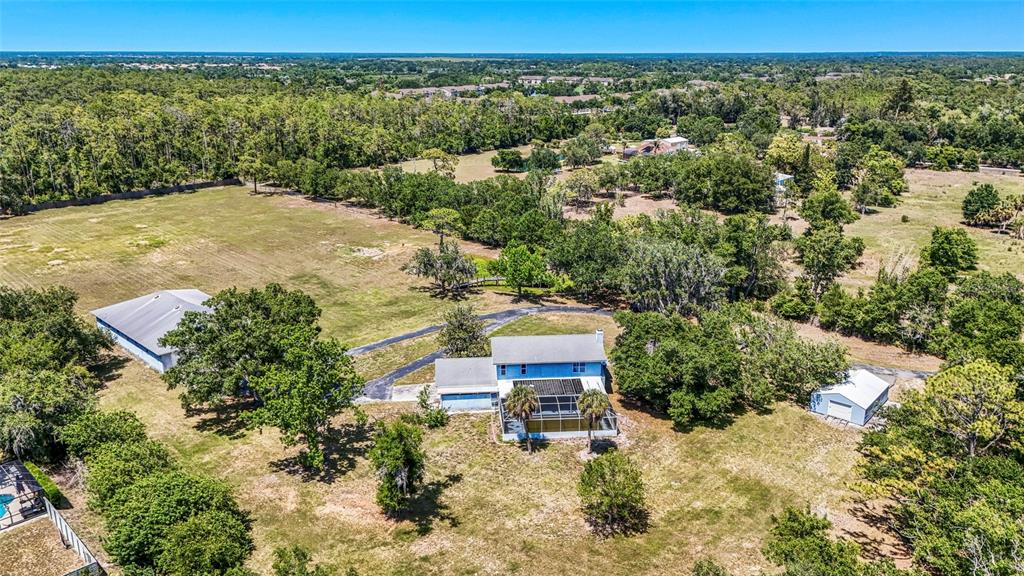 An aerial view shows a house with a pool enclosure, two outbuildings, and surrounding trees — 5650 CHURCHILL DOWNS ROAD, SARASOTA, FL