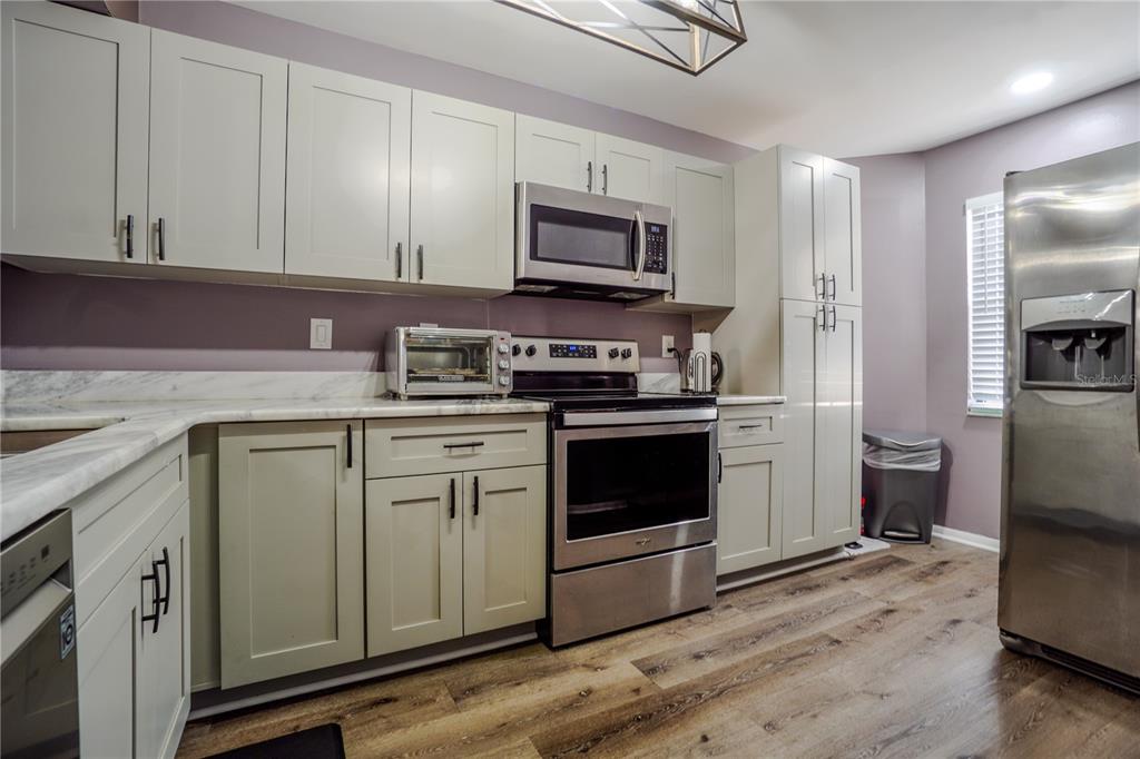 A kitchen with light green cabinets, stainless steel appliances, and wood-look flooring — 104 HIDDEN ARBOR COURT, SANFORD, FL