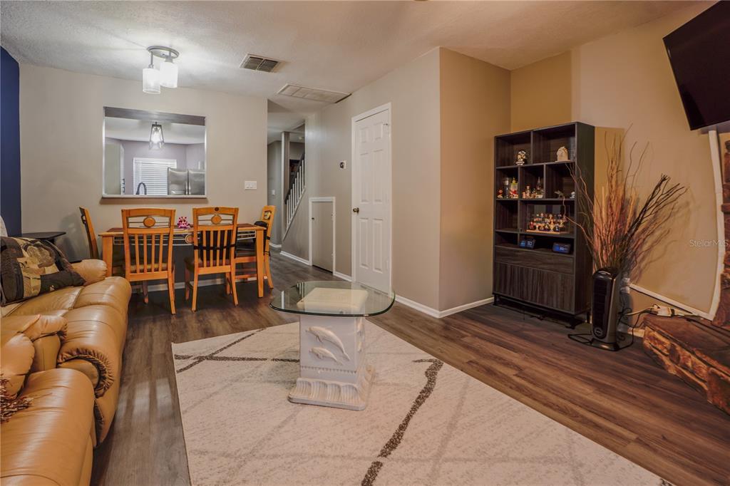 A living room with wood-look flooring, a tan leather sofa, and an adjacent dining area — 104 HIDDEN ARBOR COURT, SANFORD, FL
