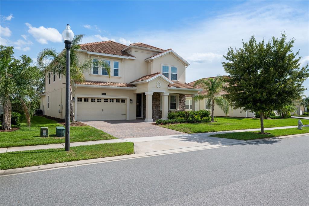 A two-story suburban house with a tan stucco exterior, stone accents, and a paved driveway — 8926 FALLEN OAK DRIVE, DAVENPORT, FL