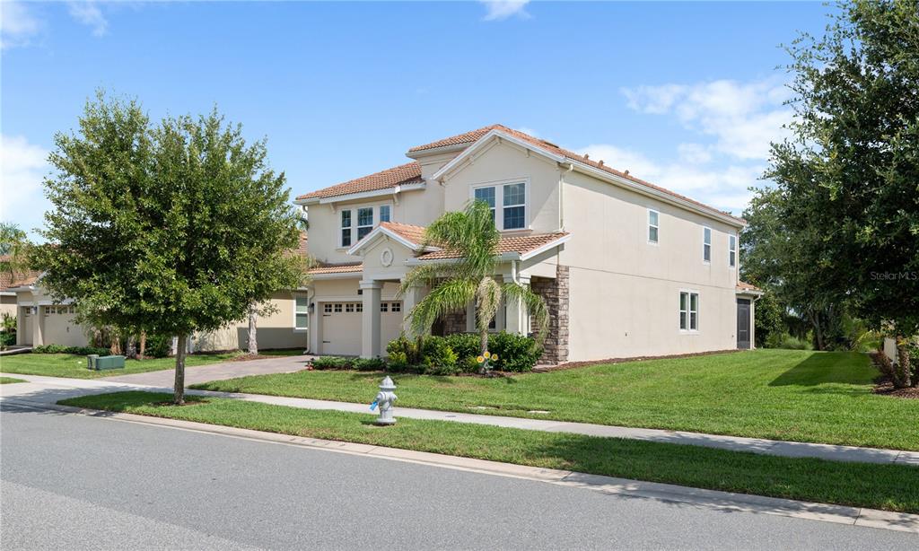 A two-story beige house with a tile roof and a front-facing garage sits on a lawn — 8926 FALLEN OAK DRIVE, DAVENPORT, FL