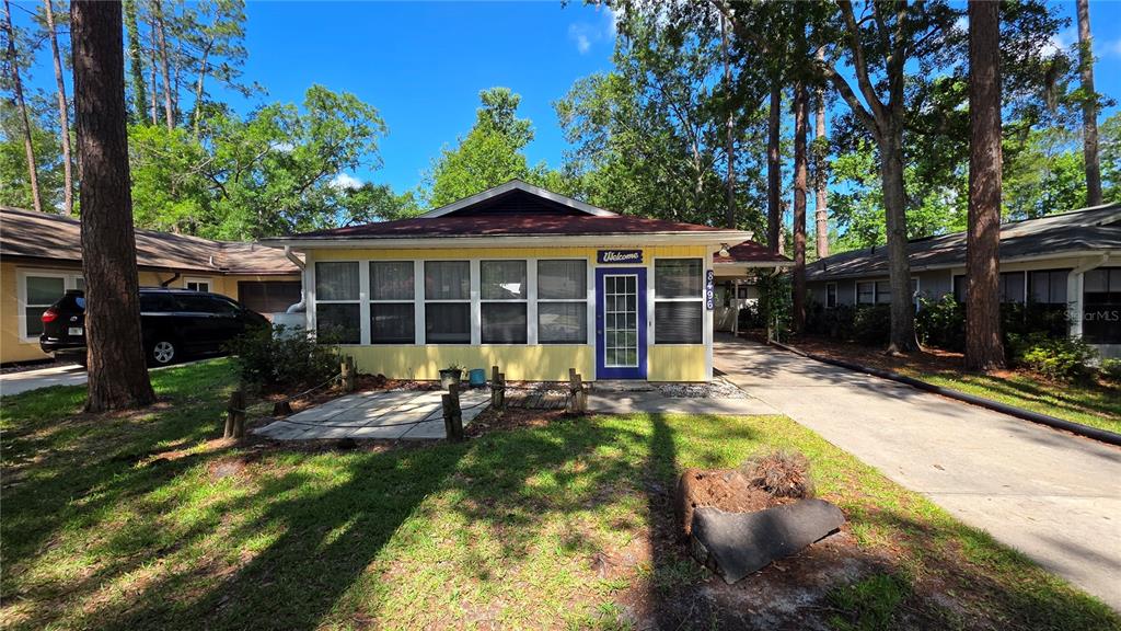 A yellow house with a screened-in front porch and a concrete driveway sits among trees — 8496 NW 38TH TERRACE, GAINESVILLE, FL