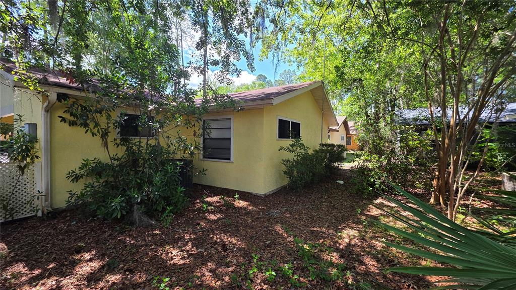 The exterior of a yellow house with a brown roof is surrounded by trees — 8496 NW 38TH TERRACE, GAINESVILLE, FL