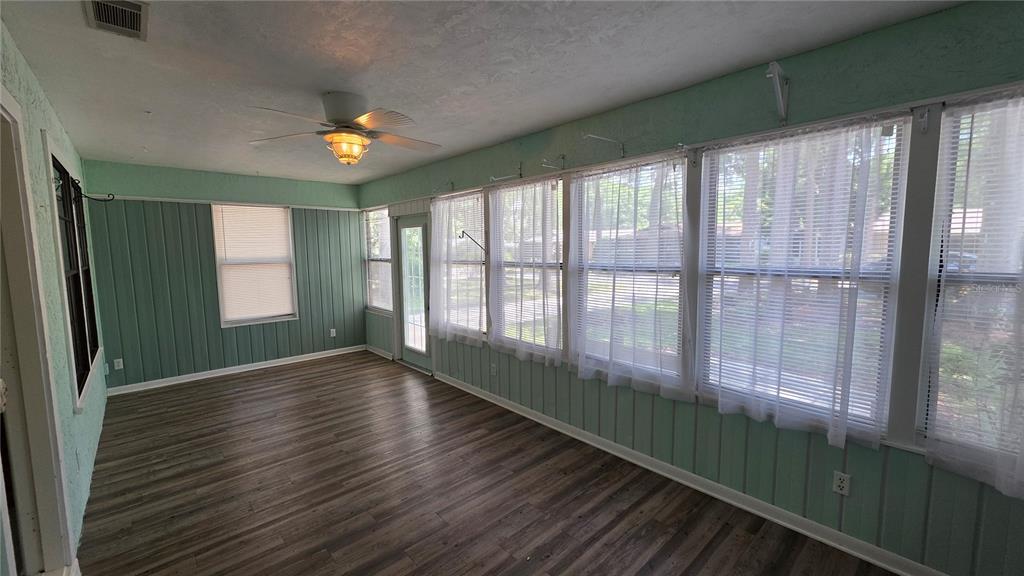 A sunroom features light green paneled walls, wood-look flooring, a ceiling fan, and large windows — 8496 NW 38TH TERRACE, GAINESVILLE, FL