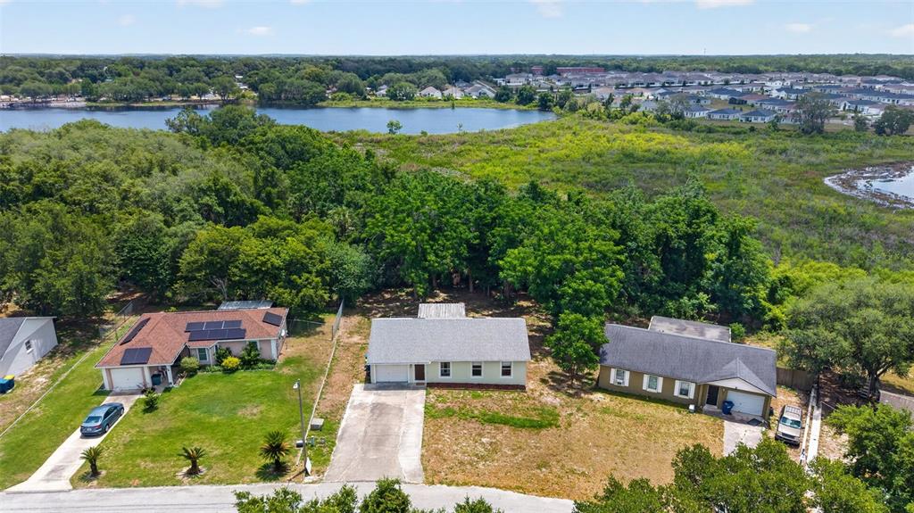 An aerial view shows three suburban houses with driveways and yards near a large lake — 36 BAY RIDGE LOOP, MASCOTTE, FL