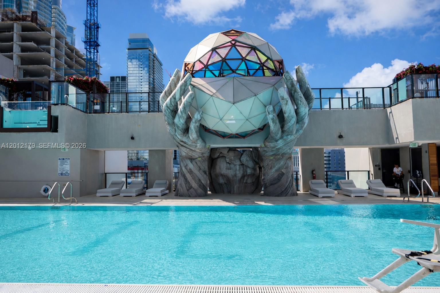 A rooftop swimming pool features a large sculpture of hands holding a geometric sphere — 20 NE 11 th st # 3403A, Miami FL 33132, MIAMI, FL